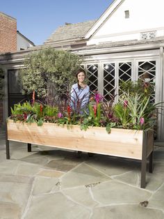 a woman standing behind a wooden planter filled with lots of flowers and greenery