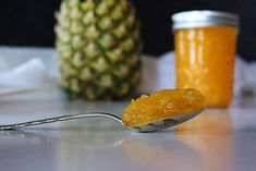 a spoon with some food on it sitting next to a pineapple and two jars