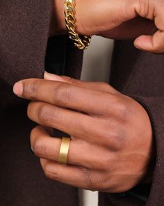 a close up of a person wearing a gold chain ring on their left hand and holding onto his jacket