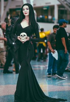 a woman dressed in black holding a skull and wearing a long sleeved dress with bow at the waist