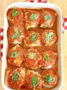 a casserole dish with tomato sauce and spinach garnished with basil leaves