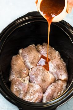 someone pouring sauce on top of some meat in a crock pot with other food items