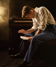 a man sitting on top of a stool next to a piano in front of a light