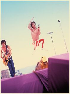 two men are performing on stage with one holding a guitar and the other jumping in the air