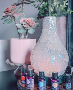 an assortment of essential oils sitting on a table next to a vase with flowers in it