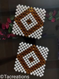 two white and brown beaded earrings sitting on top of a glass table next to flowers