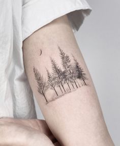 a person with a tattoo on their arm is looking at the trees in the forest