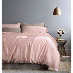 a bed with pink sheets and pillows in a room next to a lamp on a table