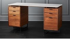 an office desk with two drawers and a marble top, in front of a gray wall