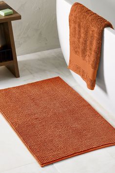 an orange bath mat sitting next to a white bath tub