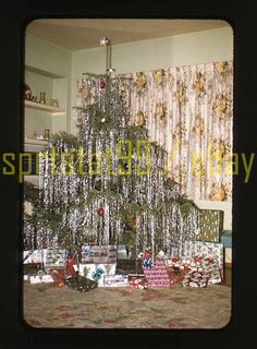 a christmas tree in the middle of a living room with presents on the floor and curtains behind it