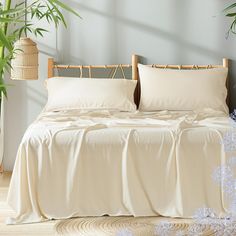 a bed with white sheets and pillows next to a potted plant in a room