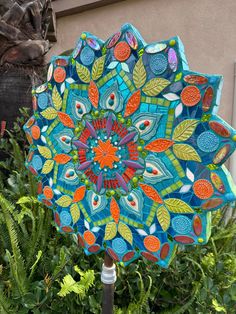 a colorful umbrella sitting on top of a lush green plant covered in lots of leaves