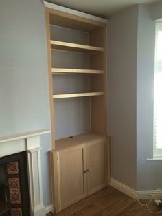 an empty living room with a fireplace and bookcase in the corner, next to a window