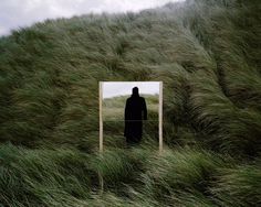 a man standing in tall grass looking at his reflection in a mirror that is reflecting him