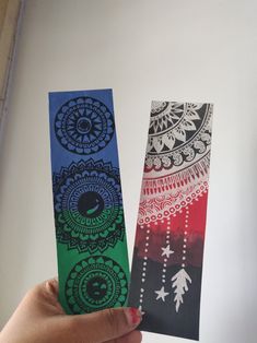 two bookmarks with designs on them being held in front of a white wall,