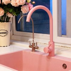 a pink kitchen sink and faucet with flowers in the window sill next to it