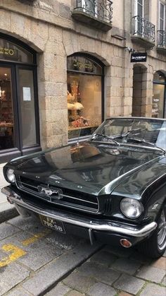 an old black mustang parked on the side of the road in front of a store