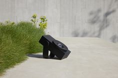 a black sculpture sitting on top of a cement ground next to green grass and bushes