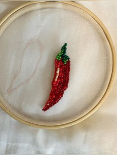 a close up of a embroidery on a hoop with a red and green beaded object