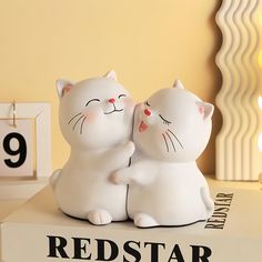 two white cats sitting next to each other on top of a book with the number nine