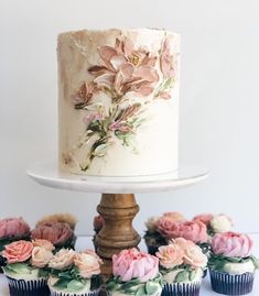 a white cake with flowers on it sitting next to cupcakes