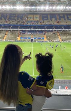 a woman holding a child in her arms at a soccer game with the stadium lights on