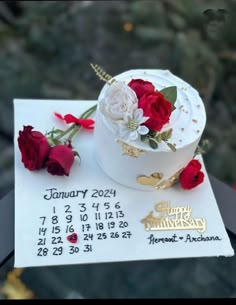 a white cake decorated with red and white flowers sitting on top of a table next to a calendar