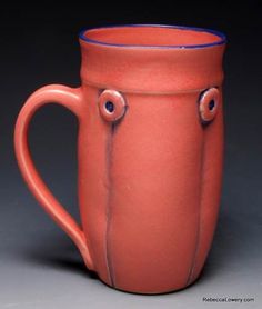 a red mug with two eyes on the outside and one in the inside, sitting on a gray surface