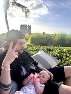 a man holding a baby while sitting on top of a couch next to a palm tree