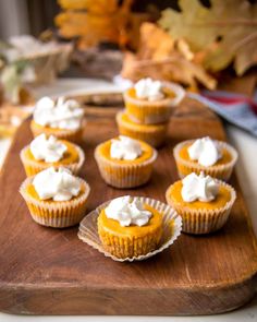 small cupcakes with frosting on a wooden cutting board next to autumn leaves