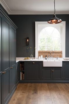 an image of a kitchen setting with sink and cabinets in dark colors on the walls