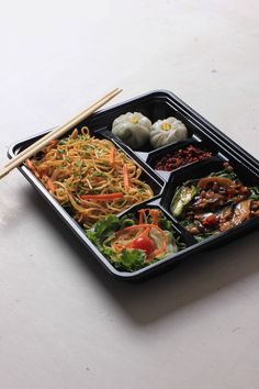 a black tray filled with different types of food and chopsticks on top of it