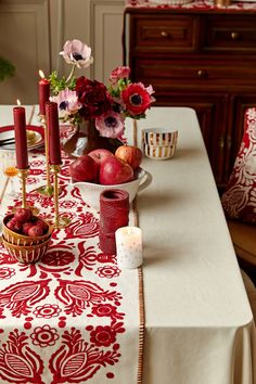 a table topped with fruit and candles on top of a white cloth covered dining room table