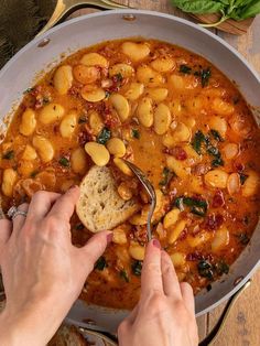 a person is spooning some food out of a pot on the table with bread