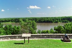 there is a bench on the side of this hill overlooking a river and trees in the distance