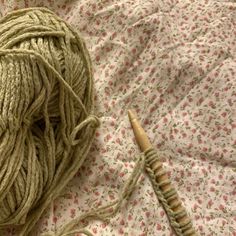 a ball of yarn next to a crochet hook on a bed sheet with flowers