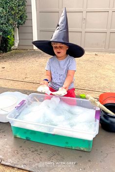 a little boy in a witches hat sitting on the ground next to a plastic container