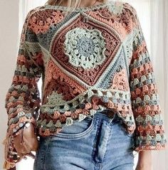 a woman is wearing a crocheted sweater and jeans