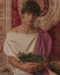 a young man dressed in roman clothing holding a bird's nest while sitting on a couch