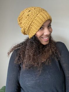 a woman wearing a yellow knitted beanie smiles at the camera while standing in front of a white wall