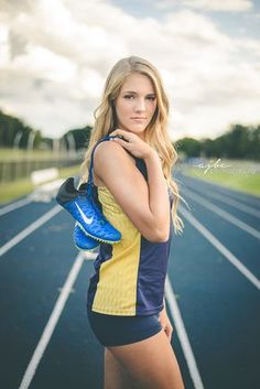 a beautiful young blond woman standing on top of a race track holding a blue bag