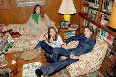 three women sitting on couches in a living room with bookshelves and lamps