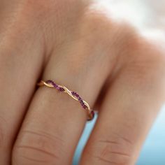 a woman's hand wearing a gold ring with pink sapphires on the band