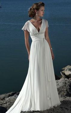 a woman in a white dress standing on rocks by the water