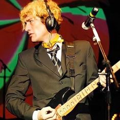 a man with headphones and a guitar in front of a microphone wearing a suit