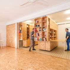 two men are standing in the middle of an empty room with bookshelves and shelves