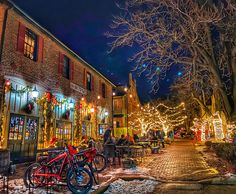 people are sitting at tables in front of buildings decorated with christmas lights