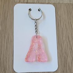 a pink letter shaped glass keychain on a white card