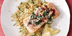 a white plate topped with salmon and rice next to a lemon wedge on top of a red table